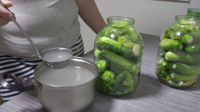 a woman pours marinade for cucumbers into jars, cooking pickles in three-liter cans, cucumber recipes
