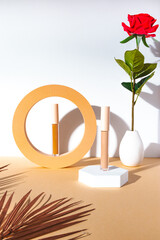 A makeup concealer in a cylindrical container with a lid sits on a hexagonal white platform. A red rose in a white vase and dried palm fronds add an elegant touch to the product photos.