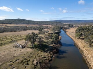 Aerial view of a serene river flowing through a grassy landscape with hills in the background
