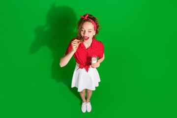 Full body photo of attractive woman top view bite cookie milk glass dressed stylish red retro clothes isolated on green color background