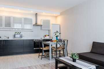 stylish interior of apartment with modern kitchen in black and white. Modern kitchen design with appliances, microwave, refrigerator, stove, sink. flowers in vase on kitchen table, chairs near table.