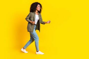 Full size photo of funny positive girl dressed khaki jacket jeans look at offer go empty space isolated on yellow color background