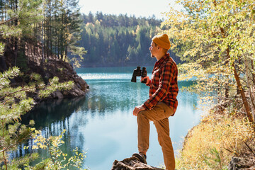 man with binoculars standing on a stone on the shore of a lake in a mountainous area Birdwatching...