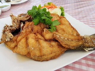 Fried sea bass with fish sauce is a popular menu item. Fried sea bass served with green coral lettuce and cucumber slices, garnished with coriander served on a table covered with a pink plaid cloth. 
