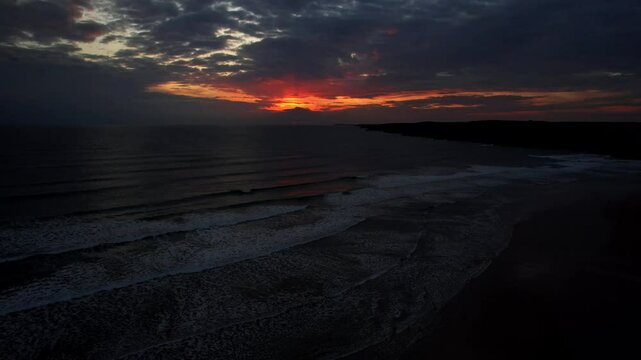 Red sunset behind dark clouds at Freshwater West Beach in Pembrokeshire, Wales. Aerial parallax