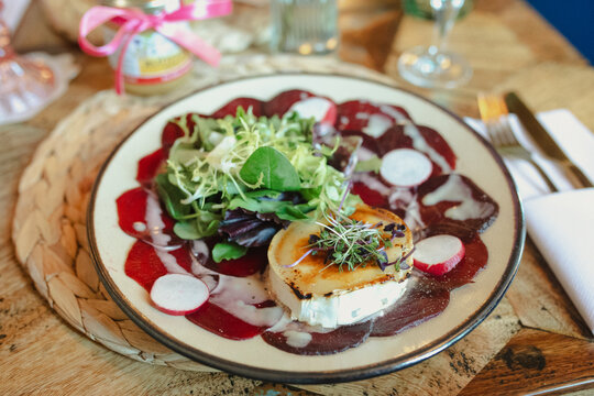 A gourmet appetizer plate featuring salad greens, goat cheese, radishes, and a beet carpaccio drizzle on a rustic wooden table.