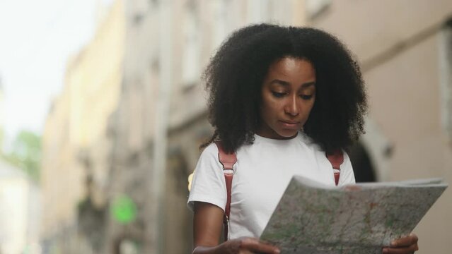 Portrait of beautiful curly young woman on the street looking for way using paper map in old town Attractive young tourist getting lost in big city trying to find route alone Time to travel