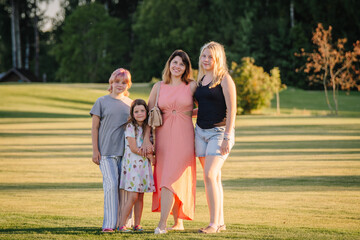 Obraz premium Valmiera, Riga - June 26, 2024 - A woman with three children posing in a grassy field, smiling and looking at the camera, with trees and a building in the background, ample copy space.