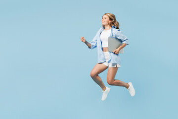 Full body young happy IT woman wears white top shirt casual clothes jump high run fast hold laptop...