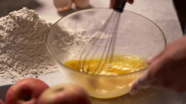 Close-up of hands whisking eggs in a bowl, preparing for baking.
