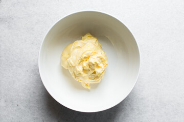 Overhead view of butter in a white mixing bowl, top view of margarine in a white bowl on a marble countertop