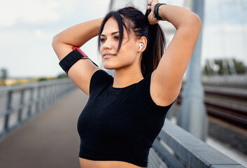 Young fitness woman in black sport outfit preparing for a run at bridge.