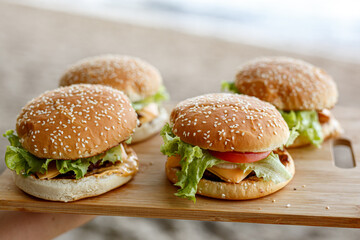Four homemade burgers on a wooden tray on a outdoor background.