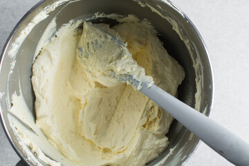 Overhead view of Cream colored american buttercream on a mixing bowl, russian buttercream in a silver bowl