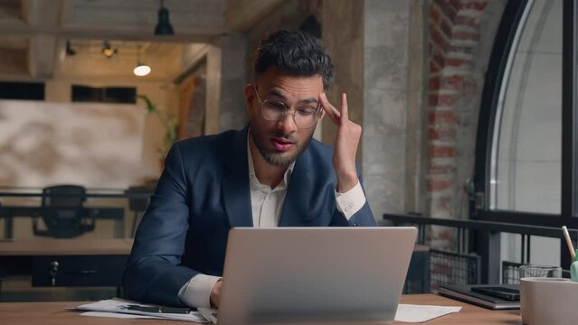 Indian Arabian man male guy business entrepreneur sad businessman at office overworked difficult job trouble working laptop computer tired exhausted feel headache suffer head pain ache health problem