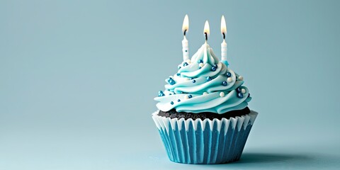 Delicious chocolate cupcake with blue frosting and lit candles on a blue background. Perfect for birthday, anniversary, or celebration images.