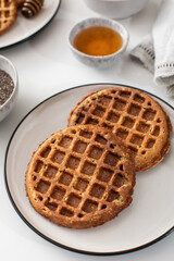 Homemade oatmeal and chia seed waffles on a white plate, accompanied by honey and ingredients