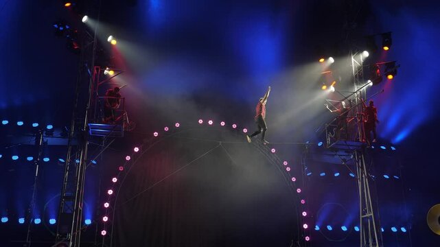 A circus show with tightrope walkers under the dome of the circus under the light of colorful spotlights and smoke. Tightrope walkers perform in a circus, walk on a tightrope without insurance.