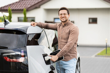 Man Charging Electric Car In Front Of Modern House