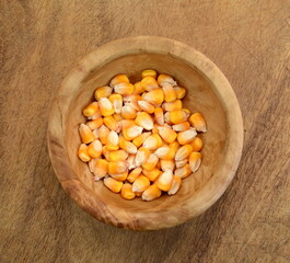 Corn seeds in a wooden bowl on wooden table, top view.