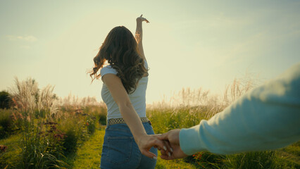 Lovely positive Caucasian couple holding hands lovers enjoying nature having fun together woman female happy wife leading man husband male following way through sunshine meadow field outdoors farmland