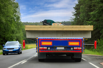 Rear view of a heavy truck and trailer transporting oversize load in highway traffic, oncoming car gives way due to the width of the transport.