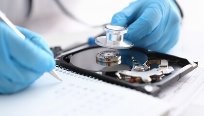 A male repairman wearing blue gloves holding stethoscope on hard drive from computer laptop in...