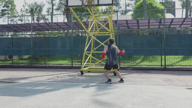 Young Asian Male Athlete Practicing Throws A Ball Into Basketball Hoop 