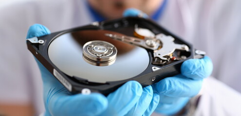 A male repairman wearing blue gloves is holding a hard drive from computer or laptop in hands....