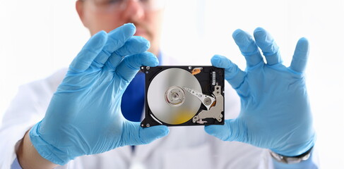 A male repairman wearing blue gloves is holding a hard drive from computer or laptop in hands....