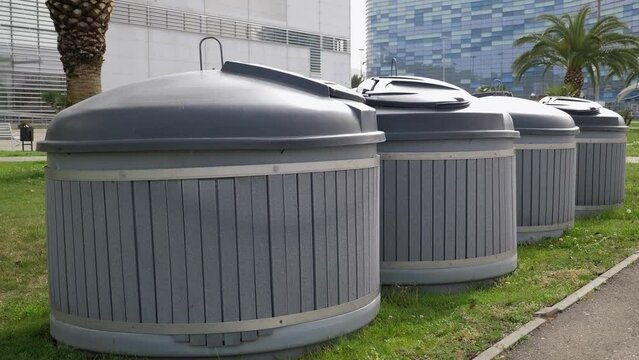 Close-up of large round garbage cans for sorting garbage in a modern park. Taking care of nature, sorting garbage. Palm trees grow in the background.