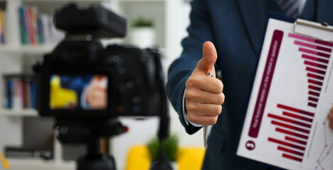 Male in suit and tie show confirm sign arm making promo videoblog or photo session in office camcorder to tripod closeup. Vlogger promotion selfie solution or finance advisor management information © H_Ko