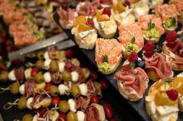 Buffet snacks. Bruschettas, canapes and sandwiches on table. Appetizers with jamon, prosciutto, salmon, cheese and olives. Italian, Mediterranean cuisine. Catering. Self-service. Close-up. Top view. 