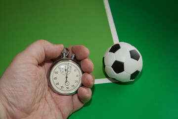 Football ball and mechanical stopwatch in hand and dollars with a football ball on a green background