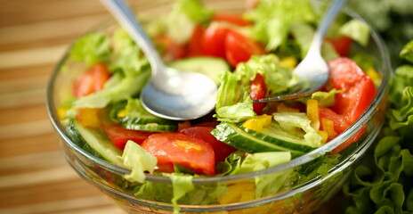 Silver fork and spoon in plate mixes salad fresh vegetables seasoned with olive oil. Raw food and vegetarian in modern society is popular concept.