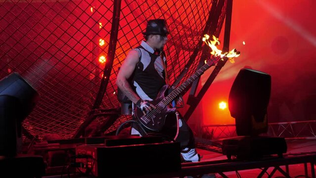 The circus actor holds a guitar in his hands, from which fire flies out. A circus show featuring acrobats, stunt riders on motorcycles in a round cage and a fire show at the circus arena.