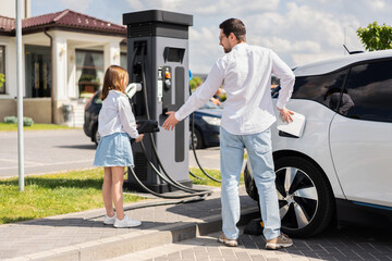 Father And Daughter Charging Electric Car At Station, Embracing Eco-friendly Lifestyle