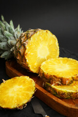 Ripe pineapple cut into slices on a wooden tray on a dark background