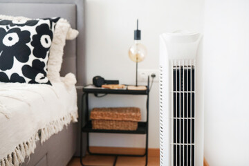 White tower fan next to a bed and bedside table with a lamp in a modern bright interior