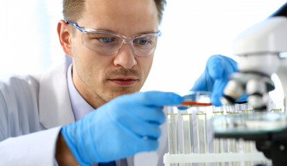 Male chemist holds test tube of glass in hand portrait overflows liquid solution potassium...