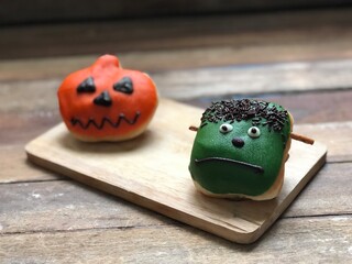 Delicious chocolate glazed donuts,decorated like a Frankenstein face and a pumpkin on wood,for...