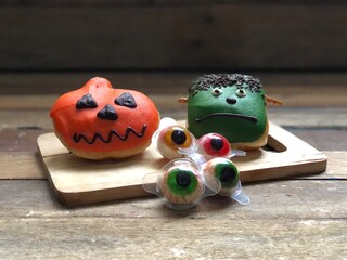 Delicious chocolate glazed donuts,decorated like a Frankenstein face and a pumpkin on wood,for funny Halloween festival,natural dimly light,free space for your text design,selective focus.