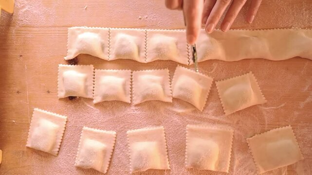 Top down flat lay view of 4k slow motion hands cutting the strip of filled pasta to make green tortelli or vegetable ravioli. Typical mediterranean vegetarian or vegan recipe