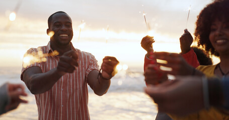 Beach, sparkler and group of people at party with happiness, celebration with friends on vacation. Crowd, smile and fireworks on island holiday in Bali for travel, together for festival at sunset