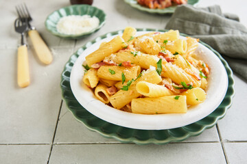 Pasta Tortiglioni or Rigatoni with bacon, parmesan cheese, pepper and basil in a retro plate on old concrete tile table background. Traditional Italian pasta recipe. Cover or article. Top view.