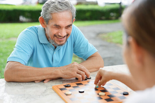 asian senior couple playing checkers game on table outdoors in the park,concept of elderly people lifestyle, entertainment,hobby,relaxation,competitive brain enhancing