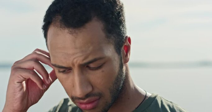 Serious young African American male with beard looking to sed and afterwards at camera. Showing his new ear phones and taking them from his ear. Looking at camera with unsatisfied face.