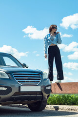 A girl in sunglasses stands by a car.