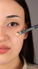 A make-up artist applies foundation to an Asian girl's face with a brush, close-up. Makeup and beauty procedure