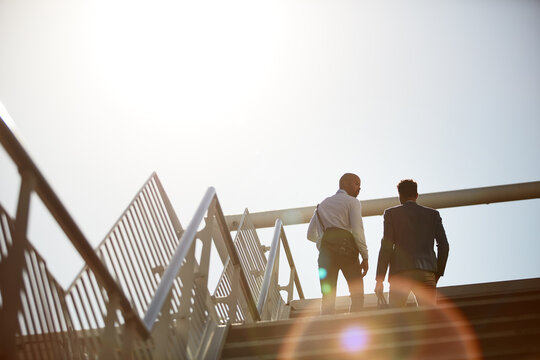 Business, men and walking on stairs in city for commute to work with communication, flare and low angle. People, back and travel together on steps outdoor for conversation, networking and partnership